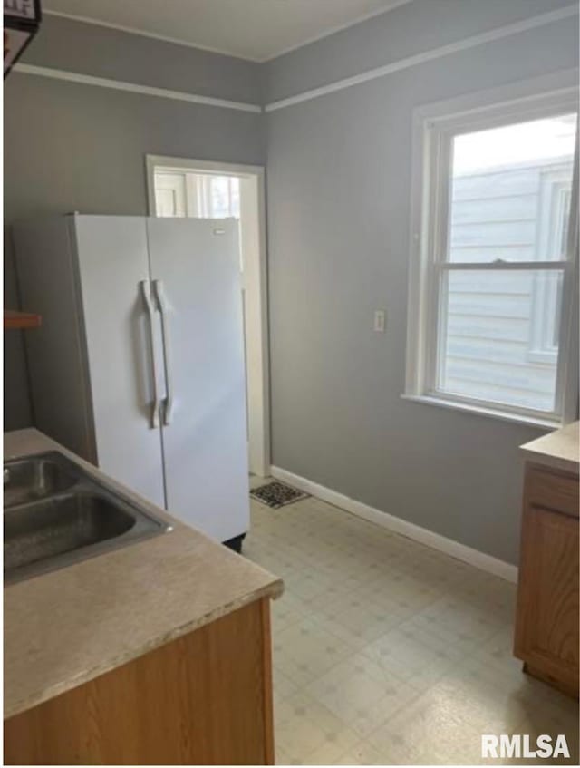 kitchen featuring a sink, baseboards, light countertops, freestanding refrigerator, and light floors