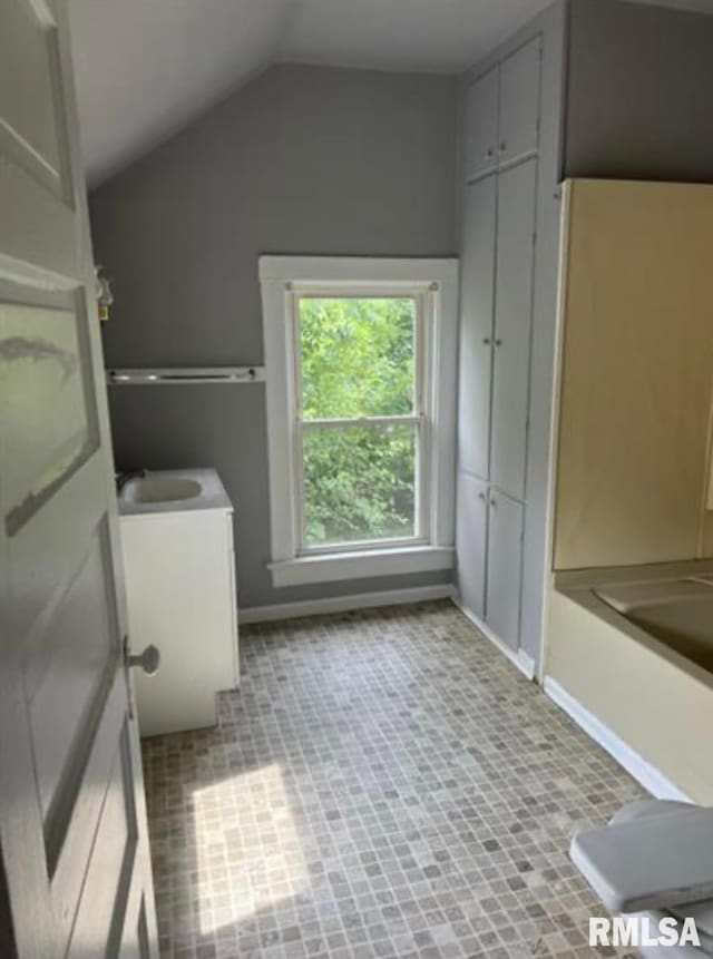 bathroom featuring baseboards, tile patterned flooring, a tub to relax in, and lofted ceiling