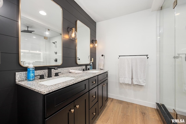 bathroom featuring double vanity, a sink, wood finished floors, and a stall shower