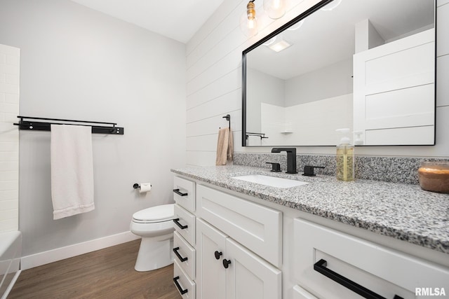 bathroom with a bath, wood finished floors, baseboards, vanity, and toilet