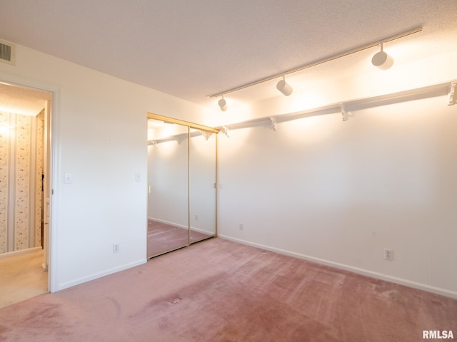 unfurnished bedroom featuring baseboards, rail lighting, carpet, and visible vents