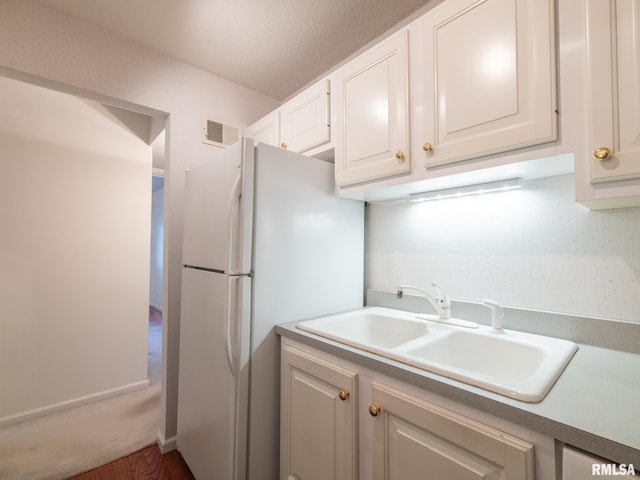 kitchen featuring a sink, freestanding refrigerator, white cabinetry, wood finished floors, and visible vents