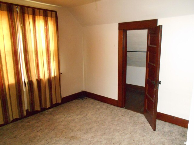 empty room with carpet flooring, baseboards, and lofted ceiling