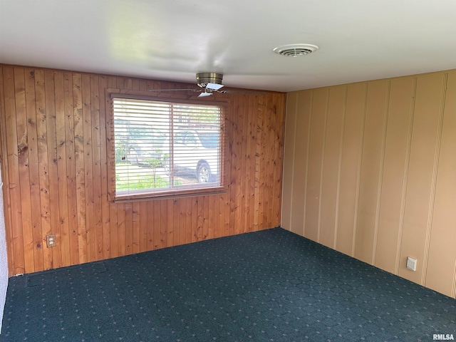 carpeted spare room featuring visible vents, wood walls, and ceiling fan