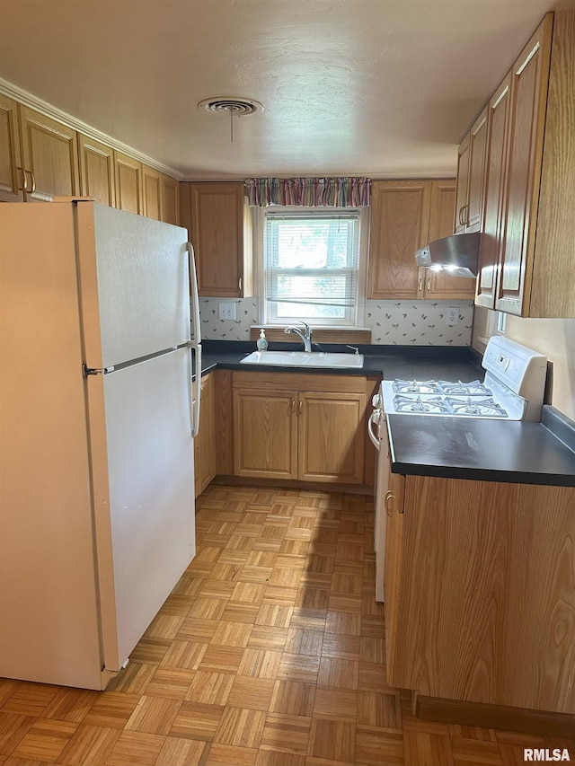 kitchen with dark countertops, a sink, stove, freestanding refrigerator, and under cabinet range hood