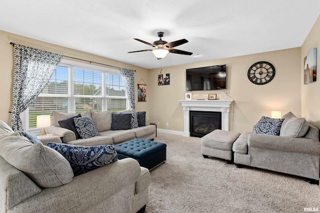 carpeted living room featuring a glass covered fireplace, baseboards, and ceiling fan