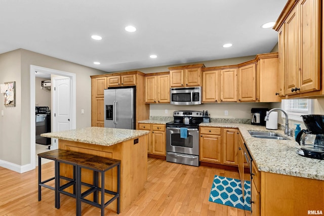 kitchen featuring a kitchen bar, a center island, a sink, light wood finished floors, and appliances with stainless steel finishes