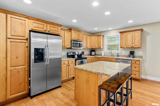 kitchen featuring light wood-style floors, a sink, a kitchen breakfast bar, and stainless steel appliances