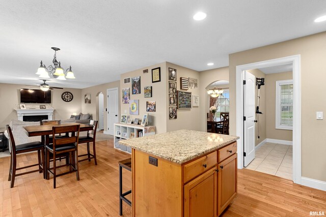kitchen with a fireplace, arched walkways, light wood-style flooring, open floor plan, and a kitchen island