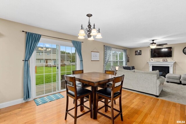 dining room featuring a glass covered fireplace, baseboards, ceiling fan with notable chandelier, and light wood finished floors