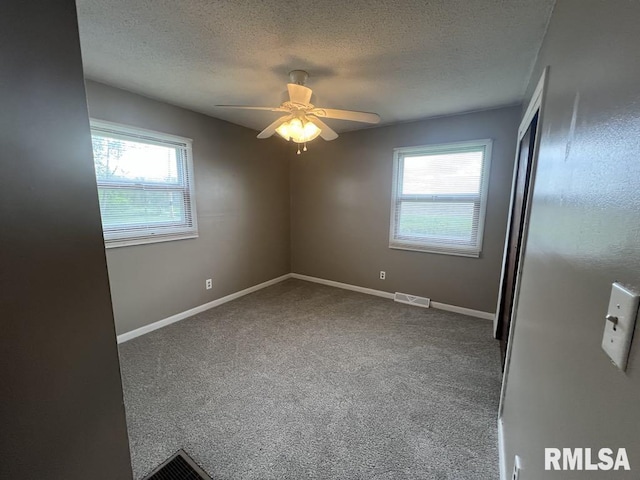 carpeted spare room with baseboards, ceiling fan, a textured ceiling, and visible vents