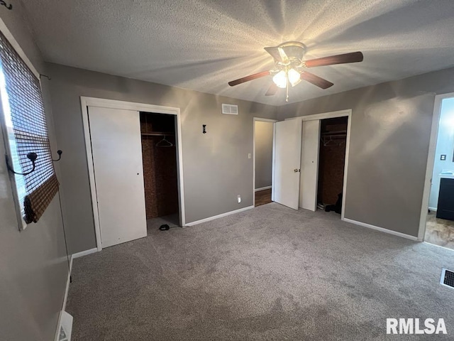 unfurnished bedroom with a textured ceiling, visible vents, baseboards, multiple closets, and carpet