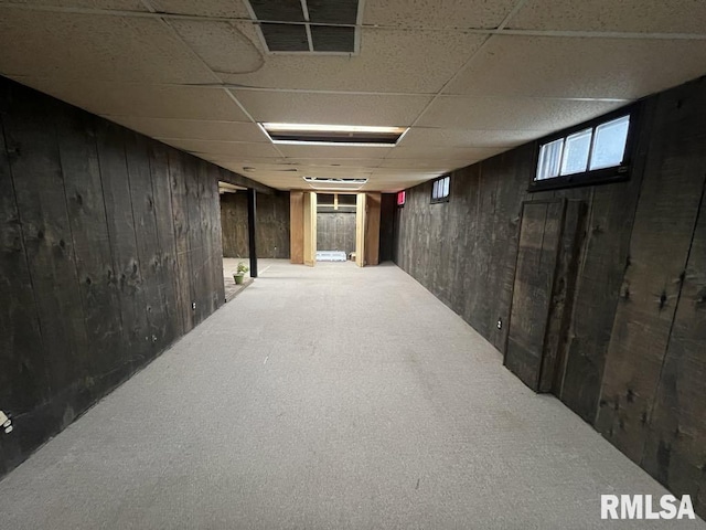 below grade area with wooden walls, visible vents, a drop ceiling, and carpet