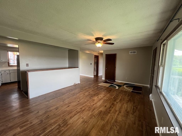 empty room with dark wood-style flooring, a textured ceiling, a ceiling fan, baseboards, and visible vents