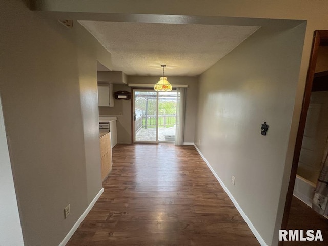 unfurnished dining area with baseboards, a textured ceiling, and dark wood-style flooring