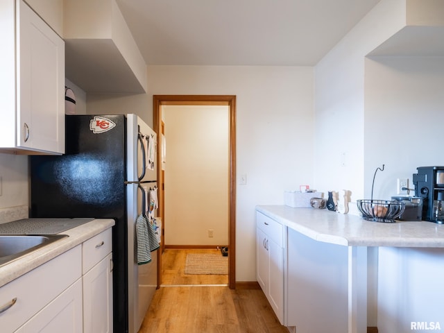 kitchen with freestanding refrigerator, light countertops, white cabinetry, a sink, and light wood finished floors