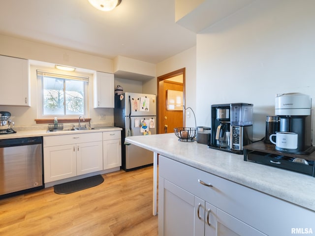 kitchen with appliances with stainless steel finishes, a sink, light countertops, white cabinets, and light wood-style floors