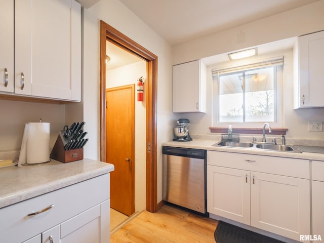 kitchen featuring stainless steel dishwasher, a sink, light countertops, light wood-style floors, and white cabinetry
