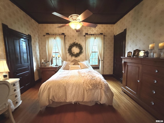 bedroom with wallpapered walls, ceiling fan, multiple windows, and wood finished floors