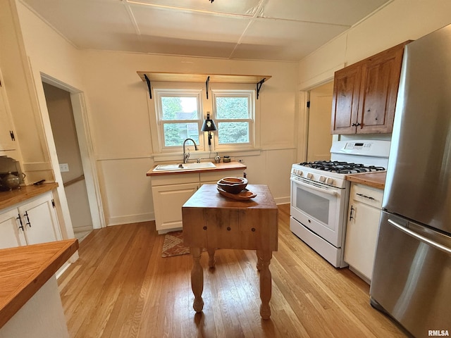 kitchen featuring freestanding refrigerator, white range with gas stovetop, light wood-style flooring, a sink, and wood counters