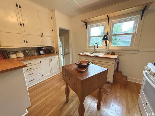 kitchen featuring a sink, stove, light wood finished floors, and white cabinetry