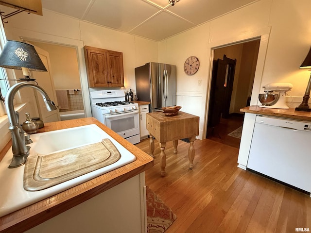 kitchen featuring brown cabinetry, white appliances, butcher block countertops, and wood finished floors