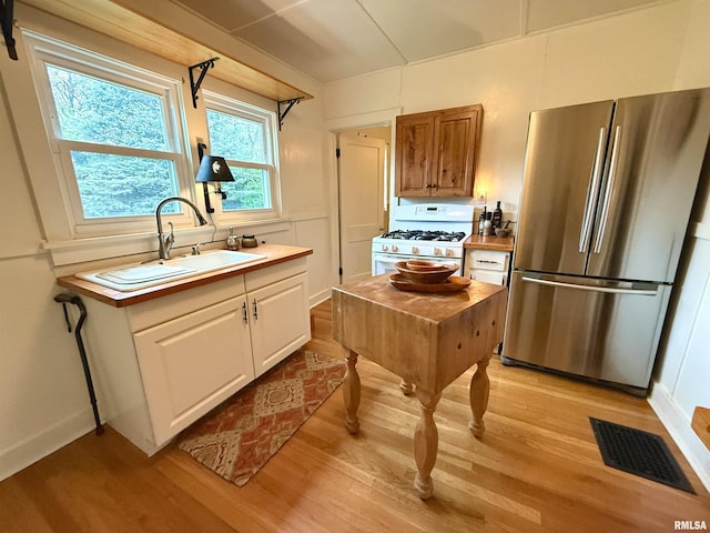 kitchen with freestanding refrigerator, visible vents, gas range gas stove, and light wood-type flooring