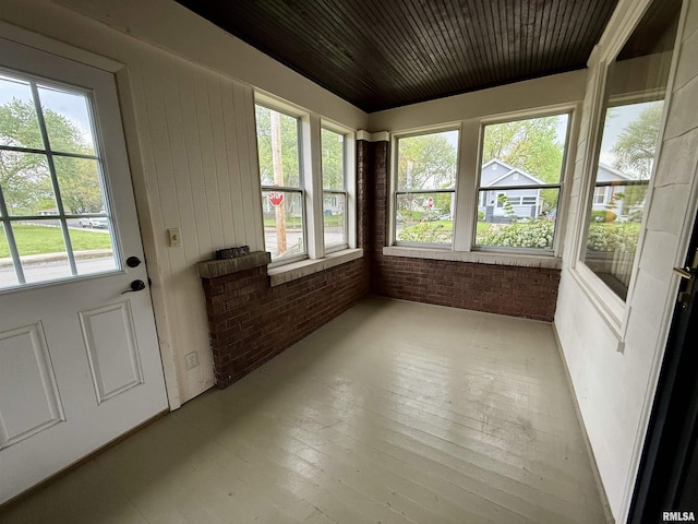unfurnished sunroom with wood ceiling, wood-type flooring, brick wall, and a wealth of natural light