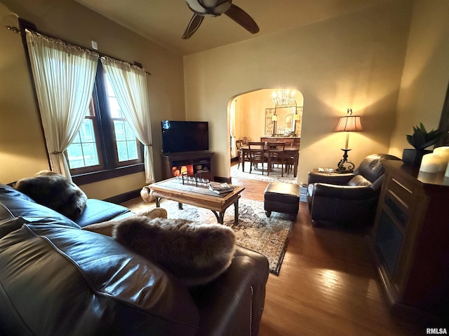 living area featuring arched walkways, wood finished floors, and ceiling fan with notable chandelier
