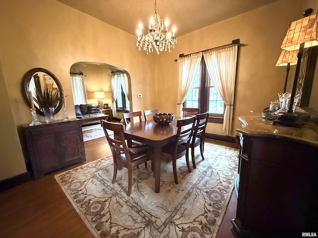dining area featuring wood finished floors, baseboards, a chandelier, arched walkways, and vaulted ceiling