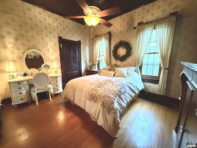bedroom featuring wood-type flooring, wallpapered walls, and ceiling fan