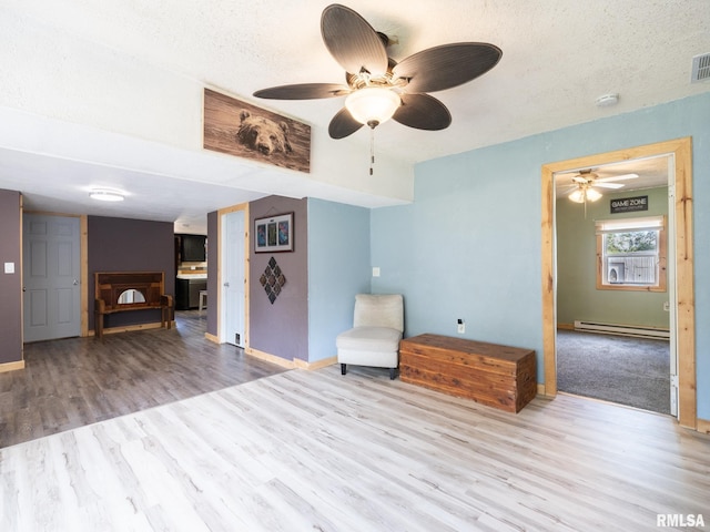 unfurnished room featuring baseboard heating, baseboards, ceiling fan, visible vents, and wood finished floors