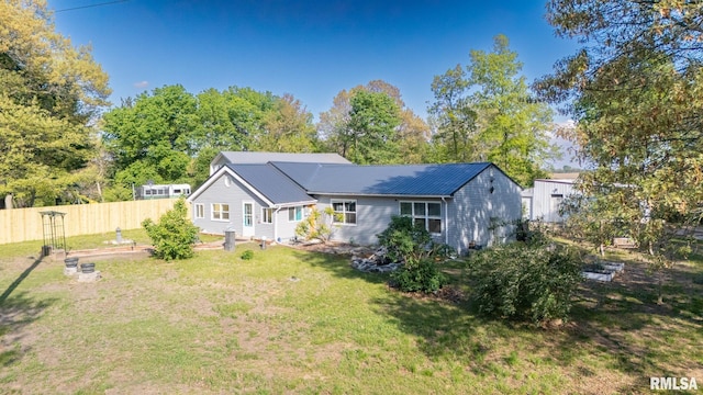 rear view of property with metal roof, fence, a vegetable garden, and a lawn