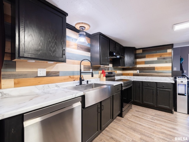 kitchen with under cabinet range hood, light wood-style flooring, dark cabinetry, and appliances with stainless steel finishes