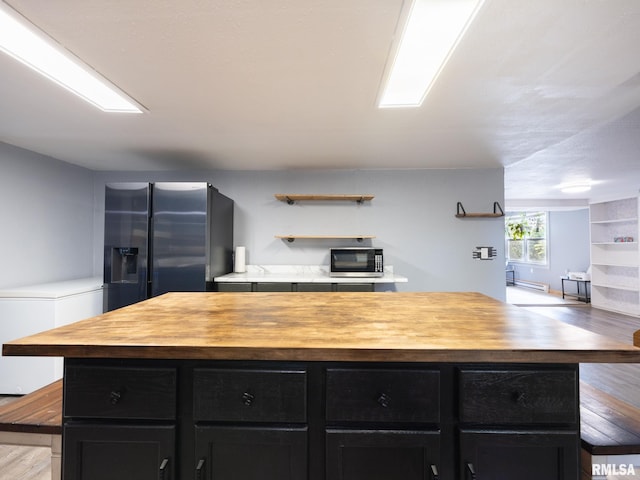 kitchen featuring butcher block countertops, stainless steel appliances, light wood finished floors, a center island, and dark cabinets
