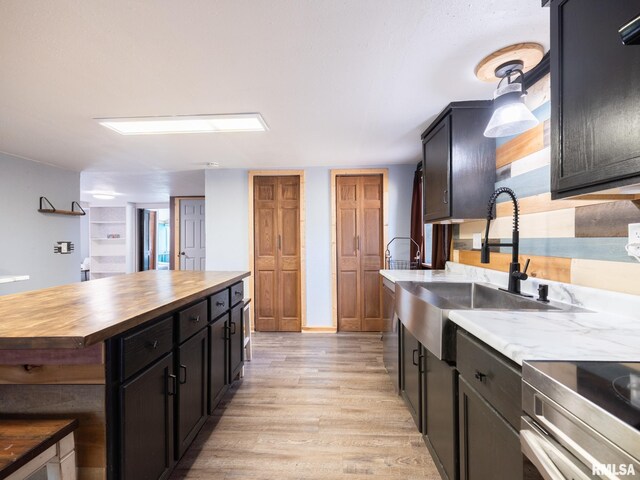kitchen with light wood finished floors, dark cabinets, a sink, wood counters, and stainless steel electric range oven