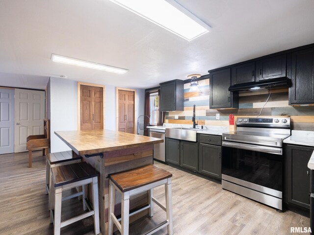 kitchen featuring a sink, light wood-type flooring, under cabinet range hood, light countertops, and appliances with stainless steel finishes