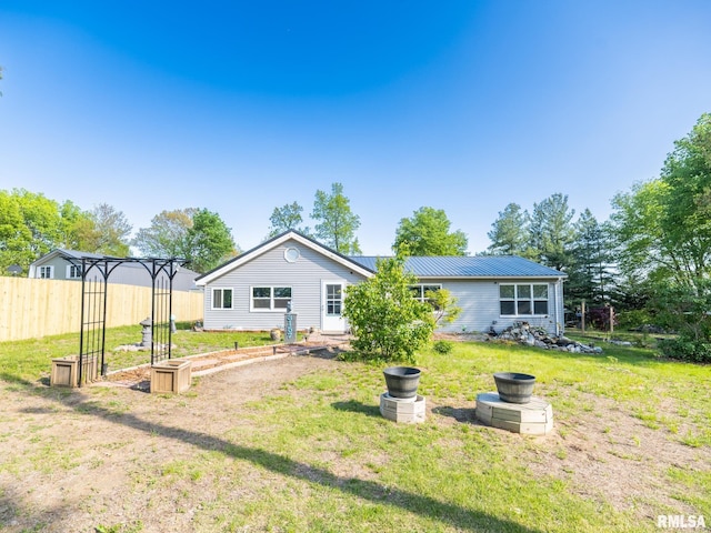 back of house with metal roof, fence, a garden, and a lawn
