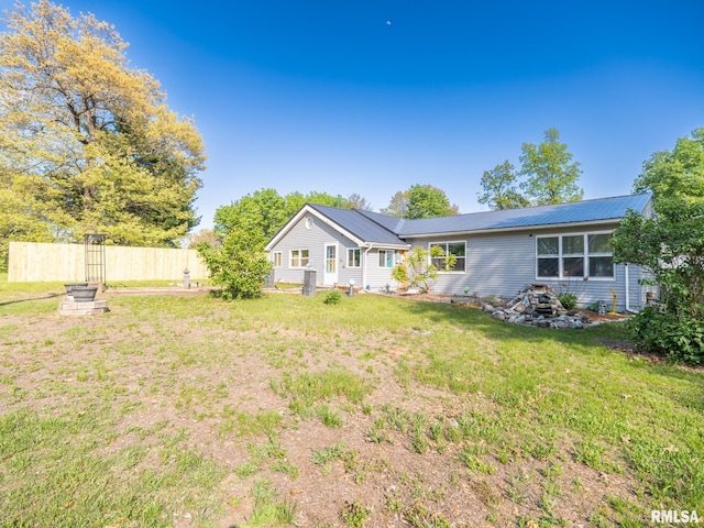 back of house with metal roof, fence, and a lawn