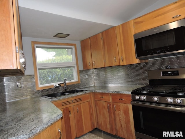 kitchen with stainless steel appliances, a sink, brown cabinetry, and backsplash
