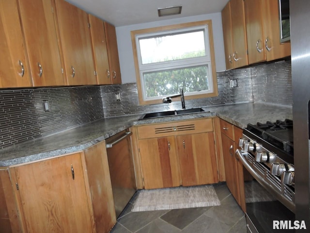 kitchen featuring a sink, appliances with stainless steel finishes, brown cabinets, dark tile patterned flooring, and backsplash