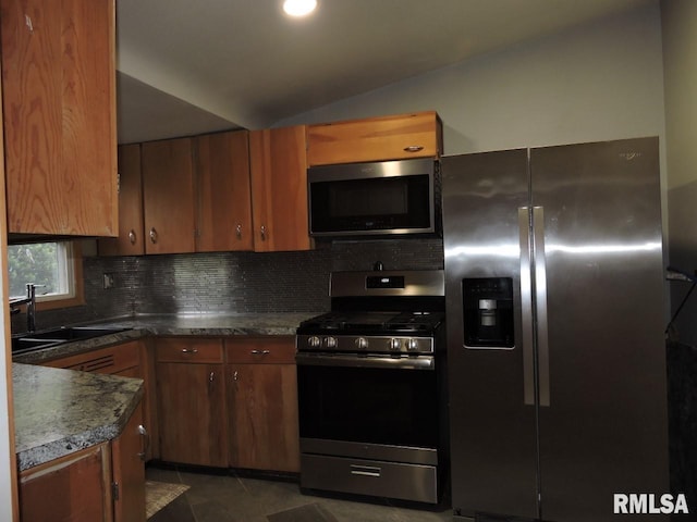 kitchen featuring stainless steel appliances, a sink, decorative backsplash, lofted ceiling, and dark countertops