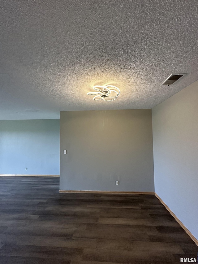 unfurnished room with visible vents, a textured ceiling, baseboards, and dark wood-type flooring