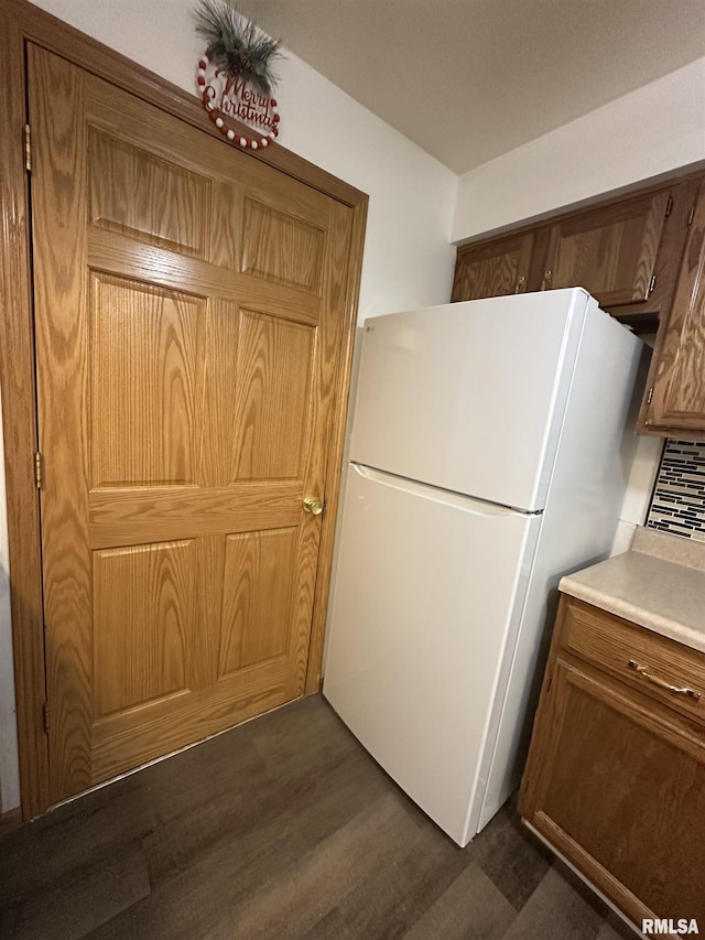 kitchen featuring freestanding refrigerator, brown cabinets, dark wood finished floors, and light countertops