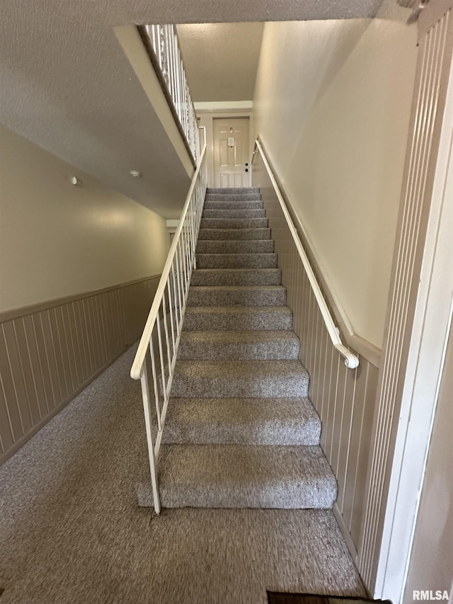 stairway featuring a wainscoted wall and carpet
