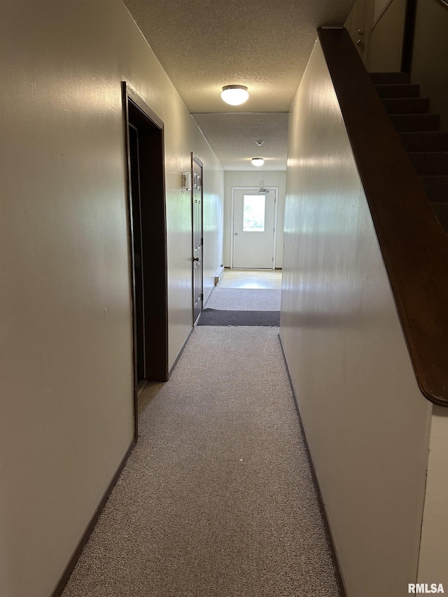 hallway featuring baseboards, light carpet, and a textured ceiling
