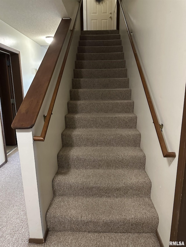 stairway featuring a textured ceiling and carpet