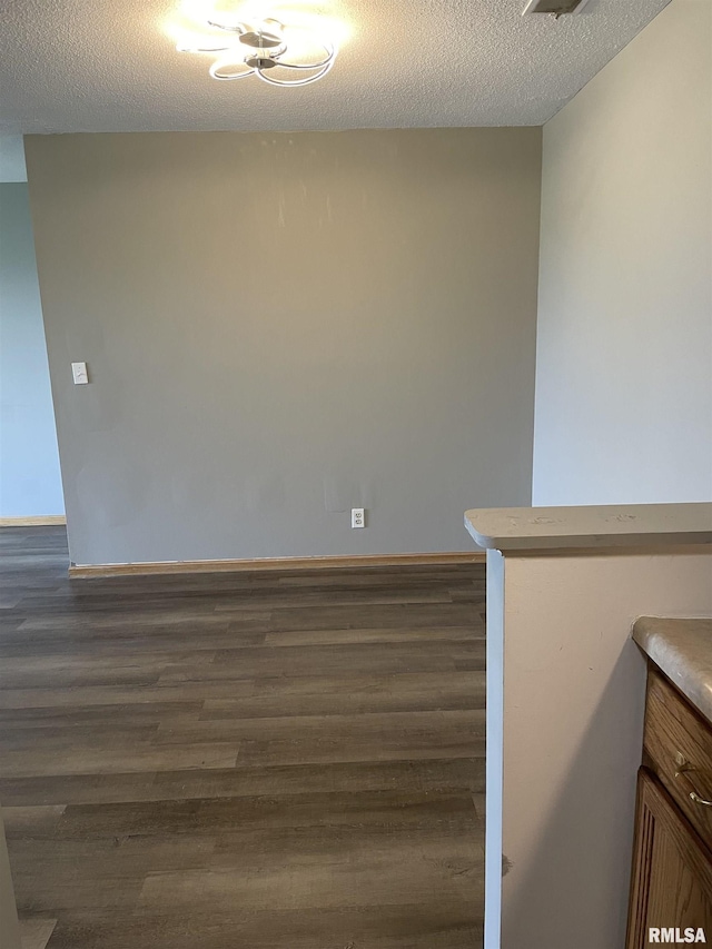 empty room featuring dark wood-type flooring, a textured ceiling, and baseboards