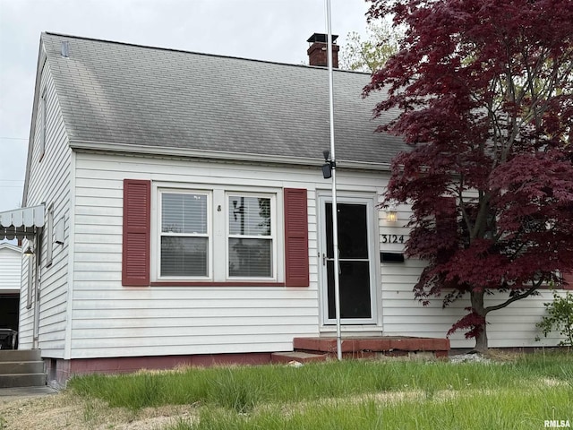 new england style home with entry steps, a chimney, and roof with shingles