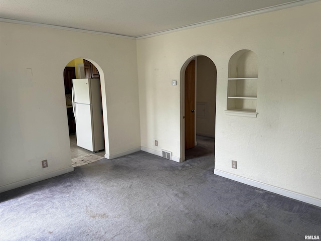 spare room with carpet floors, arched walkways, crown molding, and visible vents
